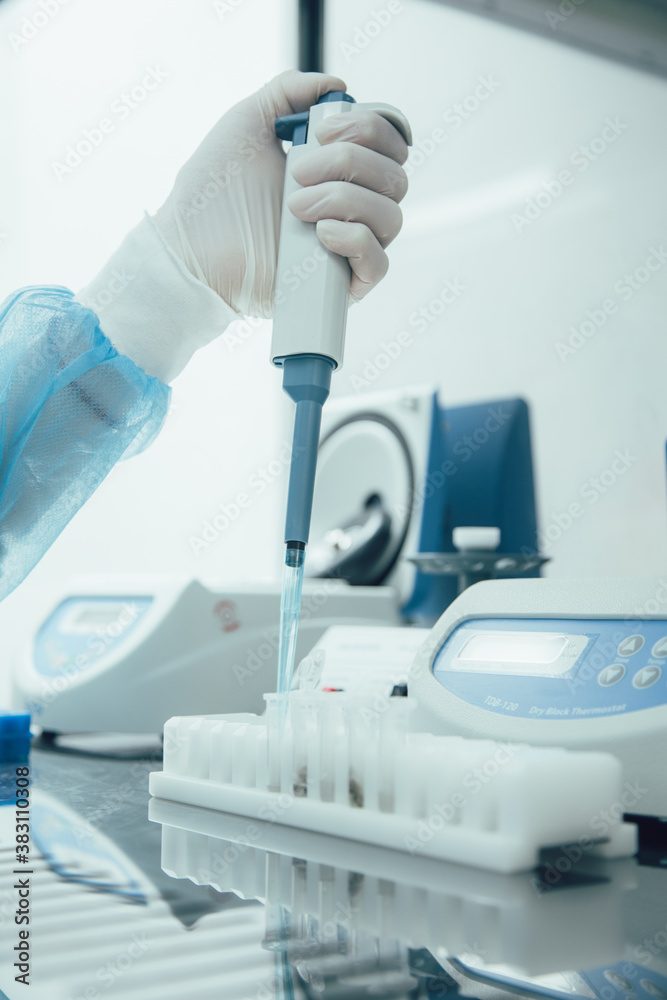 A gloved hand pipetting samples in a laboratory